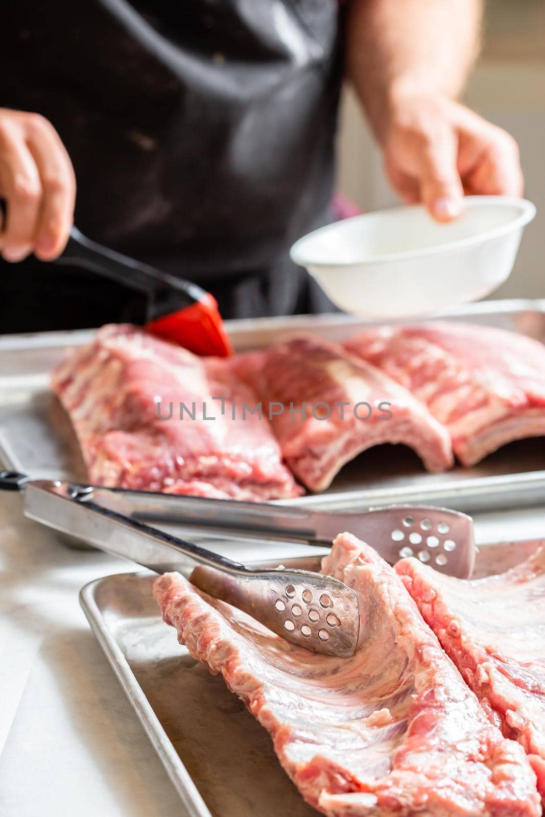 Chef brushing raw beef ribs with marinade. Male cook hands preparing meat for BBQ grilling.