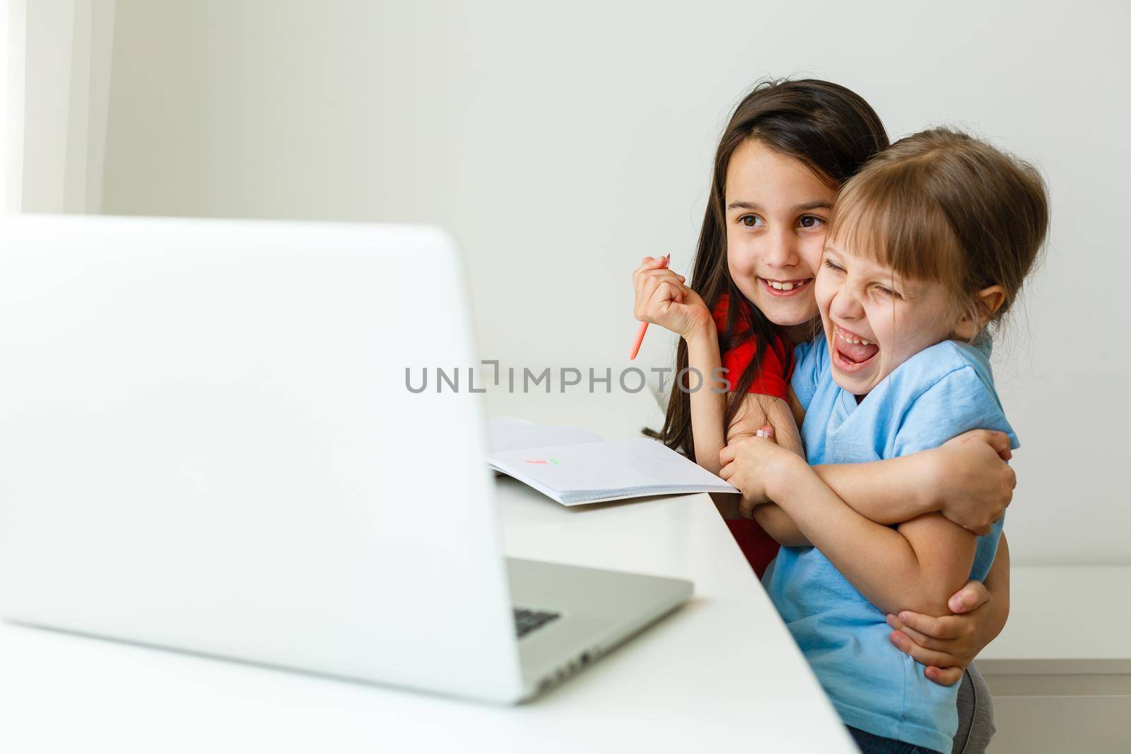 Two girls, the oldest and the youngest, are engaged at a table on a laptop.