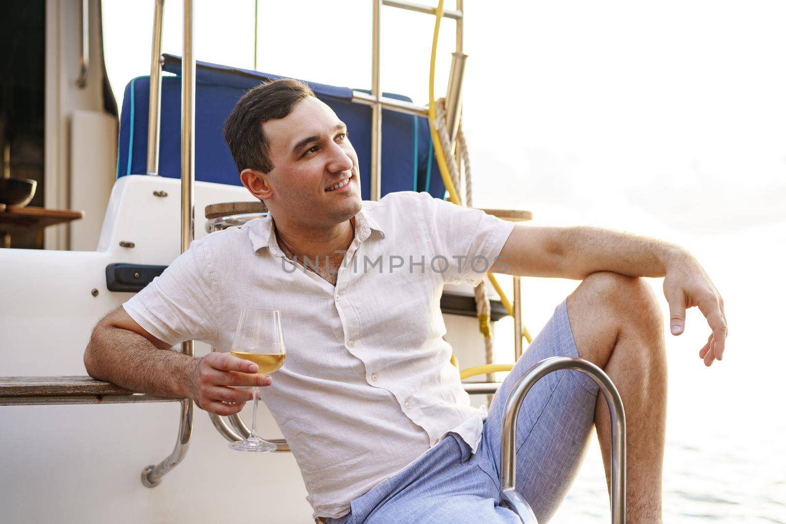 Young man holding a glass of wine on an open deck of a cruise boat, close up