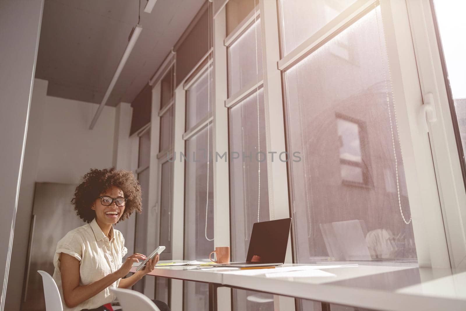 Happy pretty woman sitting at work desk and working with laptop while holding mobile phone