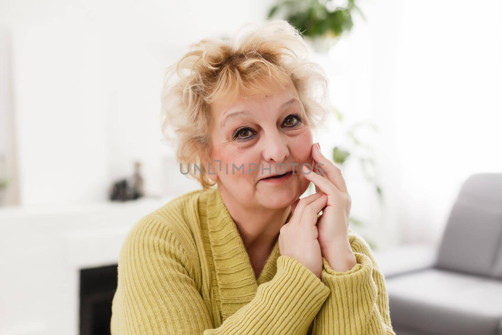Attractive elderly woman sitting on couch at home, looking at camera, makes video call, communication distantly, modern wireless technologies concept