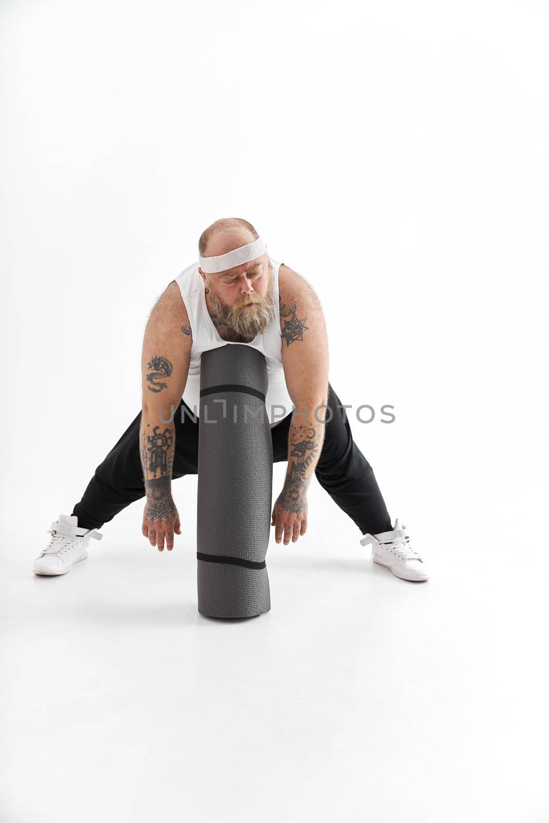 Happy fat man with big belly and tattos in sports wear with exercise mat by Yaroslav_astakhov