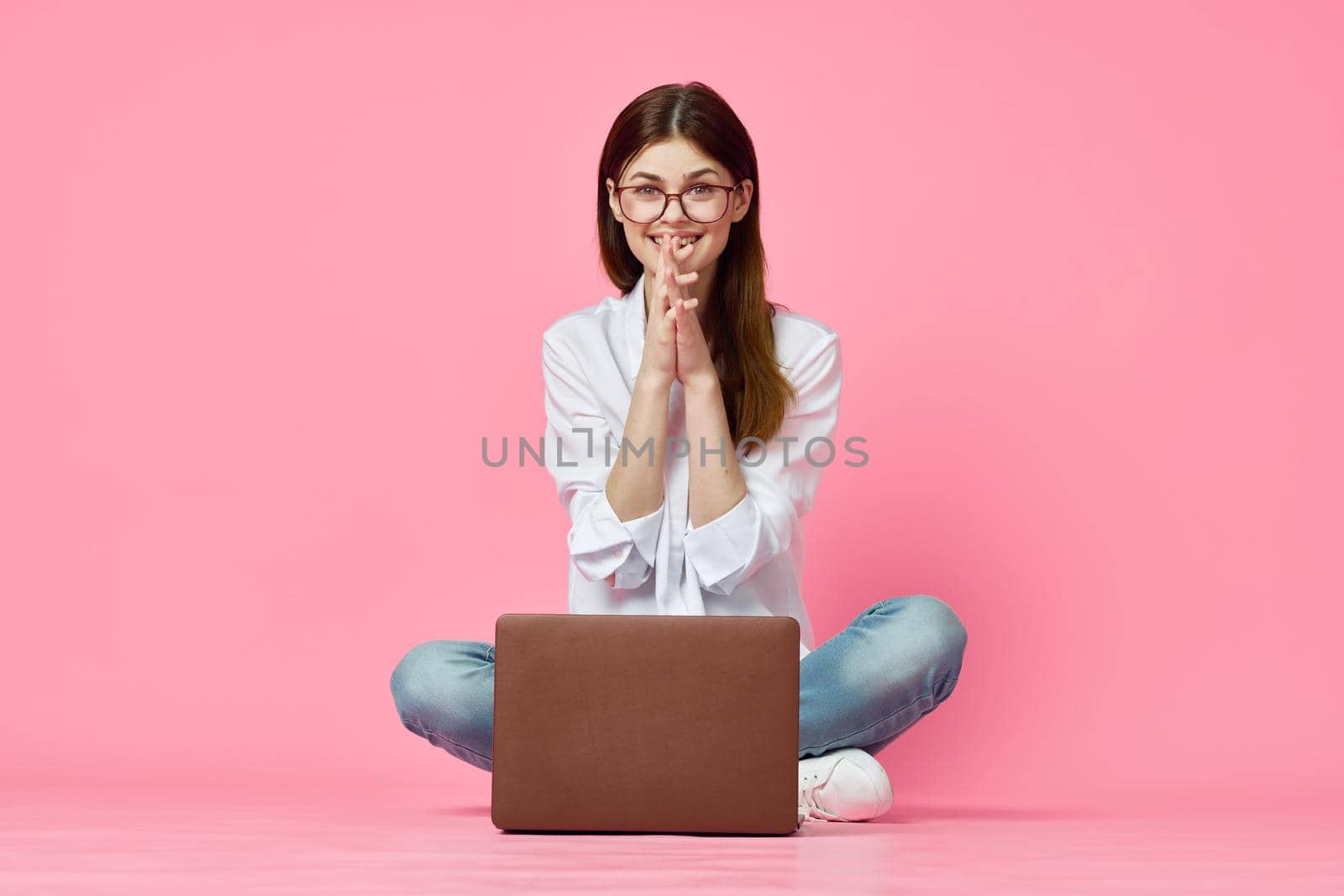 cheerful woman with laptop sitting on the floor on a pink background. High quality photo