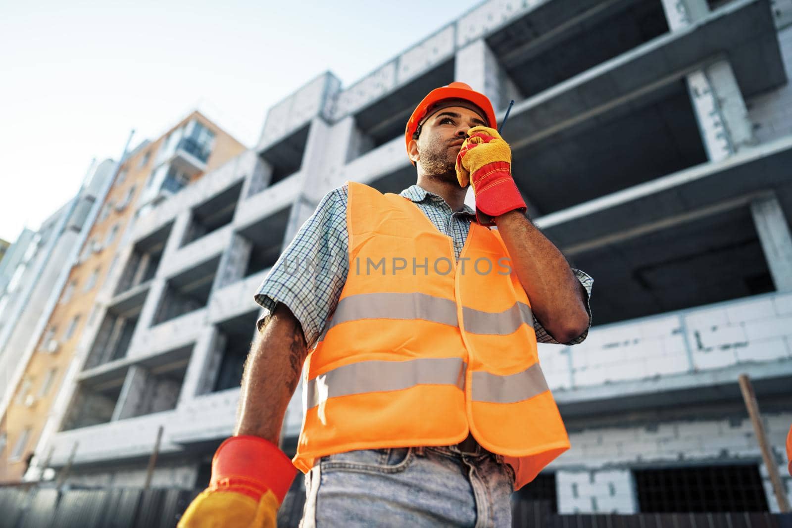 Young construction worker in uniform using walkie talkie on site by Fabrikasimf