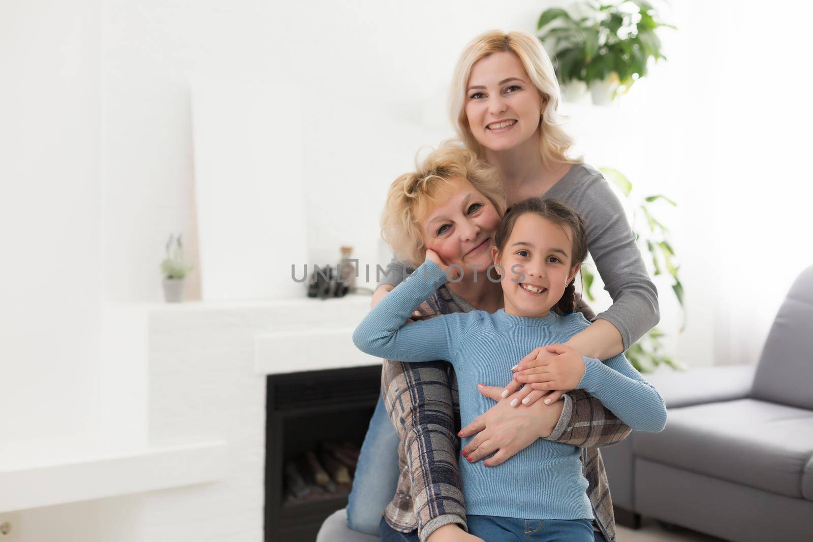 Three generations of women. Beautiful woman and teenage girl are kissing their granny while sitting on couch at home