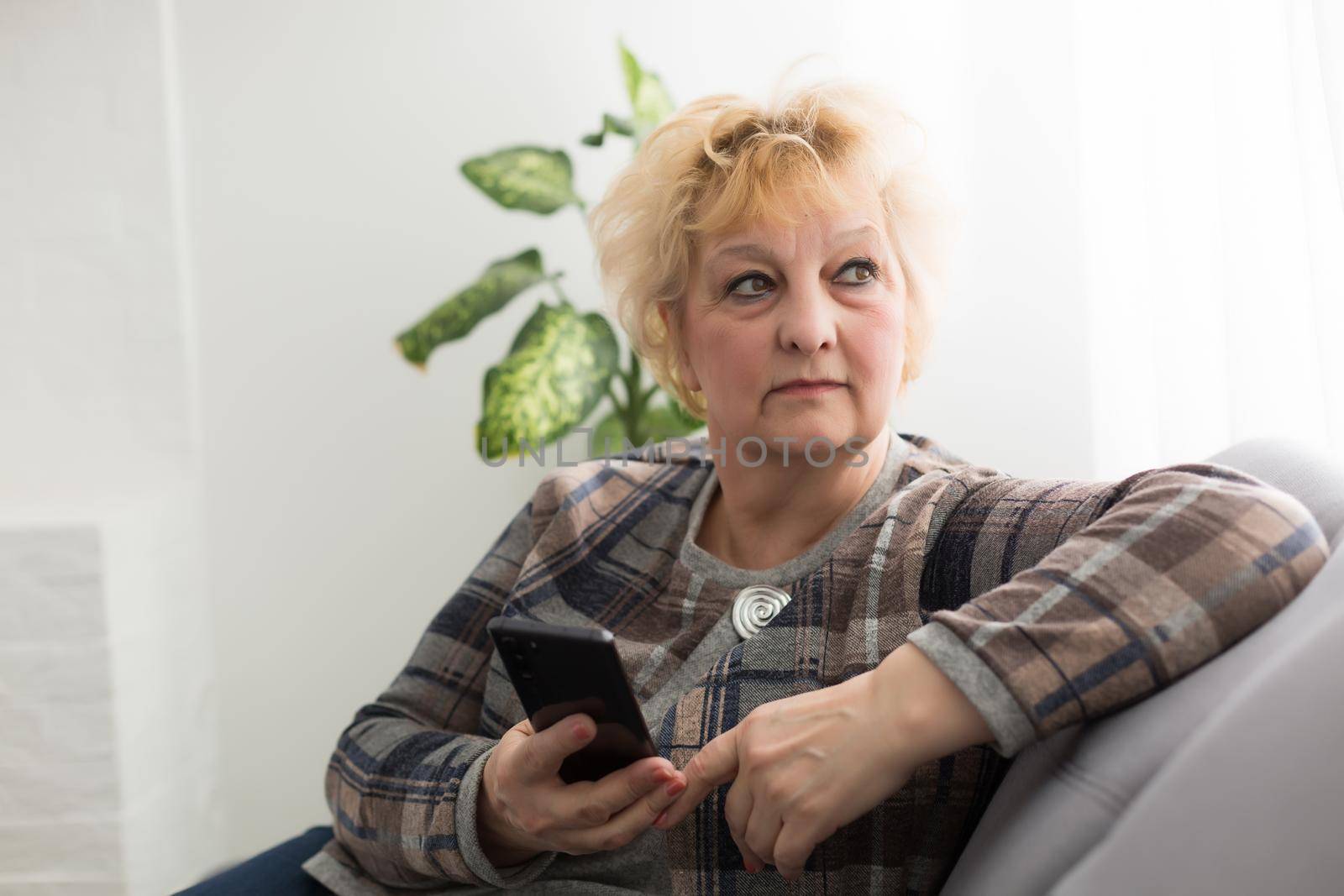 Concept of easy, fast usage of modern technology among all ages. Portrait of confident mature woman with wrinkles she is using her modern smartphone for sending a message isolated on gray background