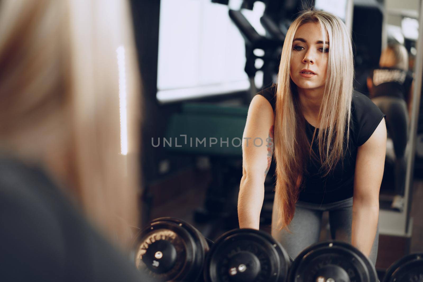 Back view of a young woman training her hands with a dumbbell in a gym