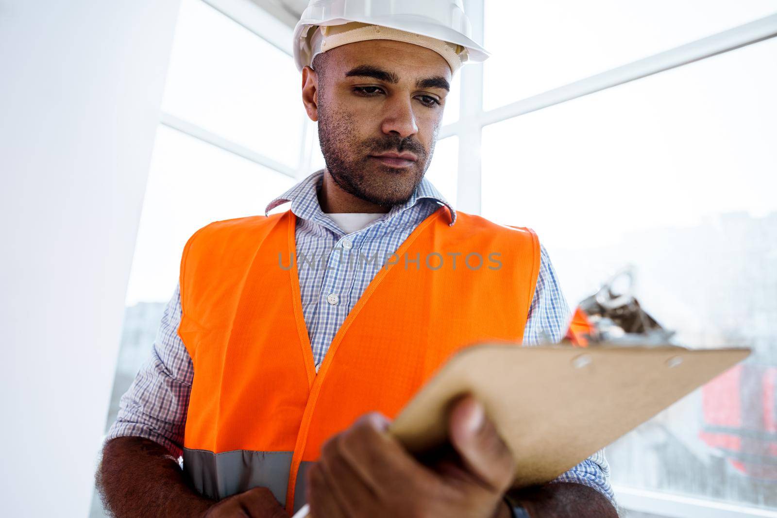 Foreman at work on construction site checking his notes on clipboard by Fabrikasimf