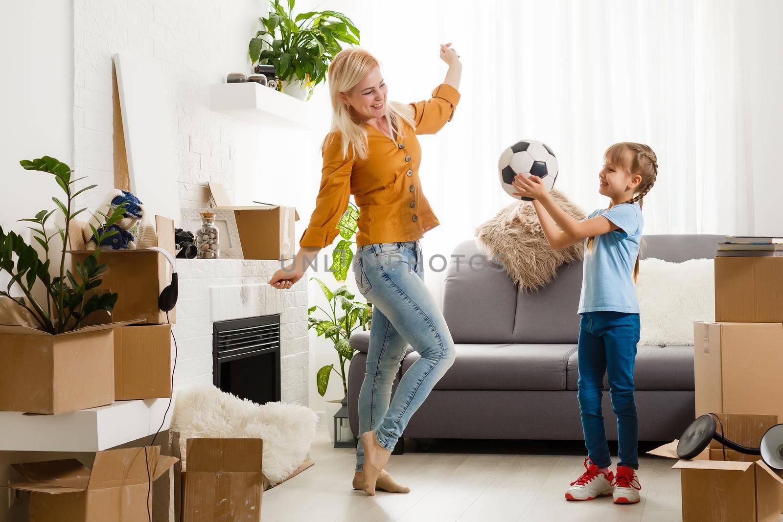 Pretty young mother and her cute little daughter having fun in new apartment and unpacking moving boxes