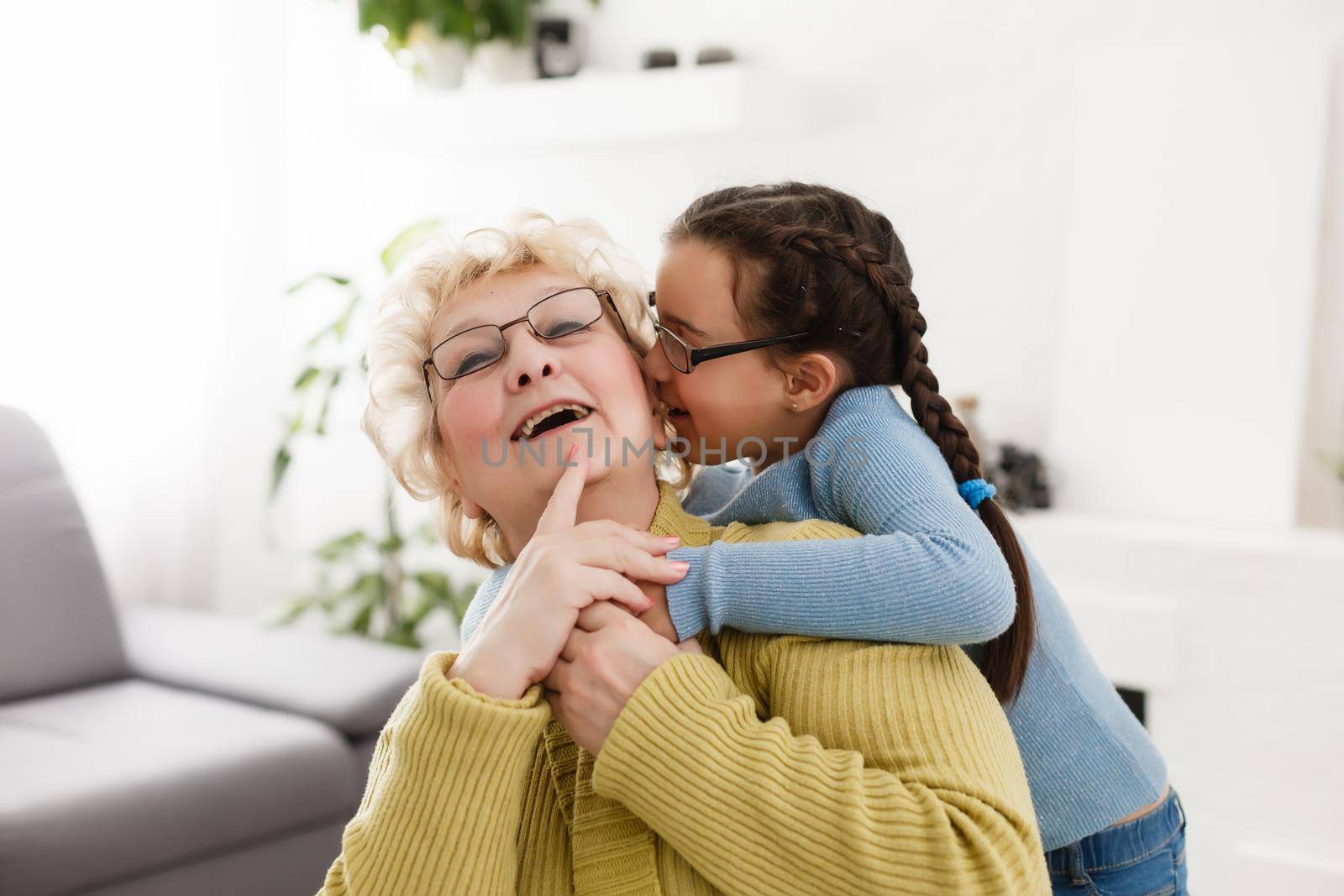 Senior woman hugging granddaughter while sitting on sofa at home