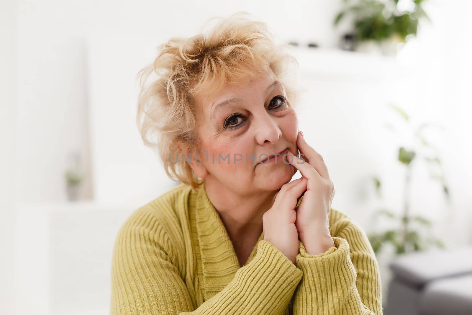 Smiling middle aged mature grey haired woman looking at camera, happy old lady posing at home indoor, positive single senior retired female sitting on sofa in living room headshot portrait