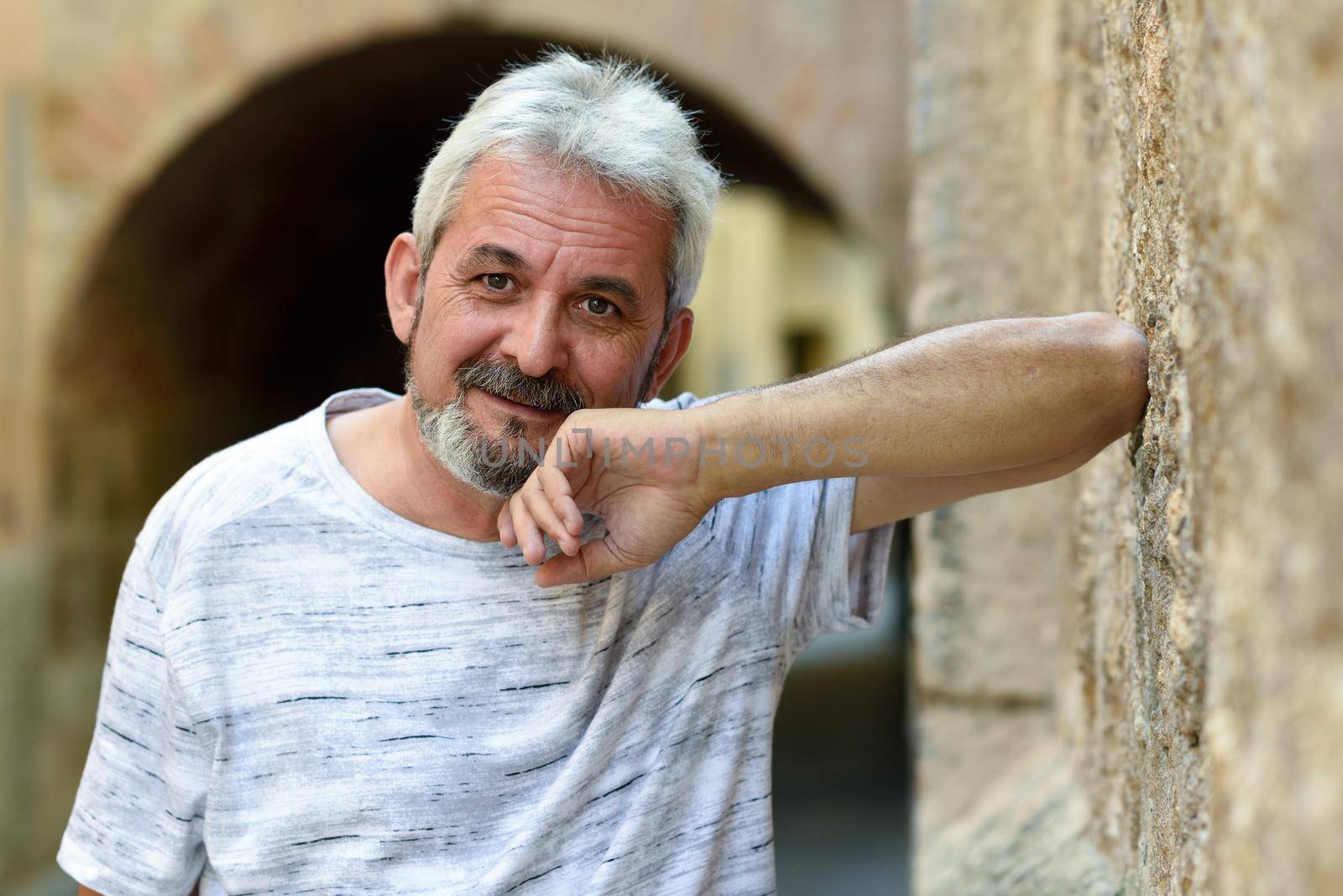 Portrait of a mature man looking at camera in urban background. Senior male with white hair and beard smiling wearing casual clothes.