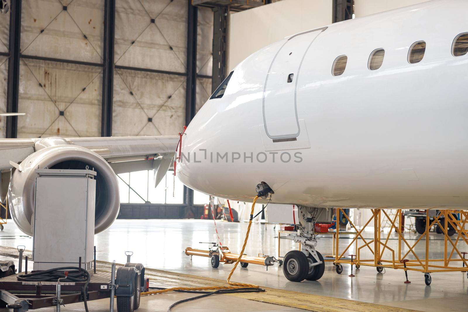 Modern new white passenger airplane on maintenance repair check in airport hangar indoors by Yaroslav_astakhov