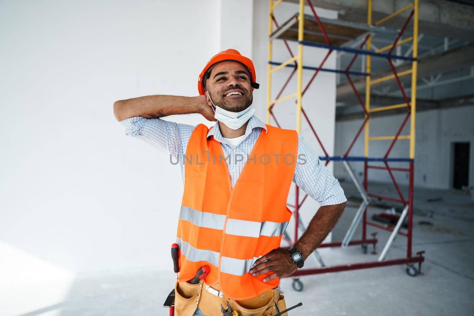 Portrait of mixed race man builder in workwear and hardhat wearing medical mask, close up by Fabrikasimf
