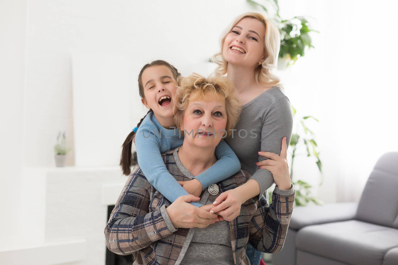 Three generations of women. Beautiful woman and teenage girl are kissing their granny while sitting on couch at home by Andelov13