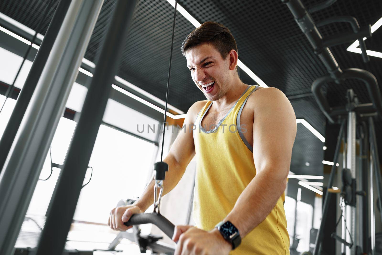 Young bodybuilder doing heavy weight exercise for biceps in a gym by Fabrikasimf