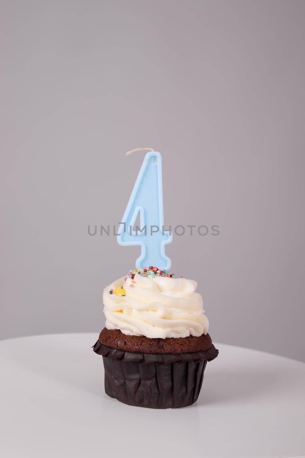 tasty chocolate cupcake with white topping cream and candle in shape of number four 4. on a white stand on a gray background. sweets, bakery. party food. dessert.