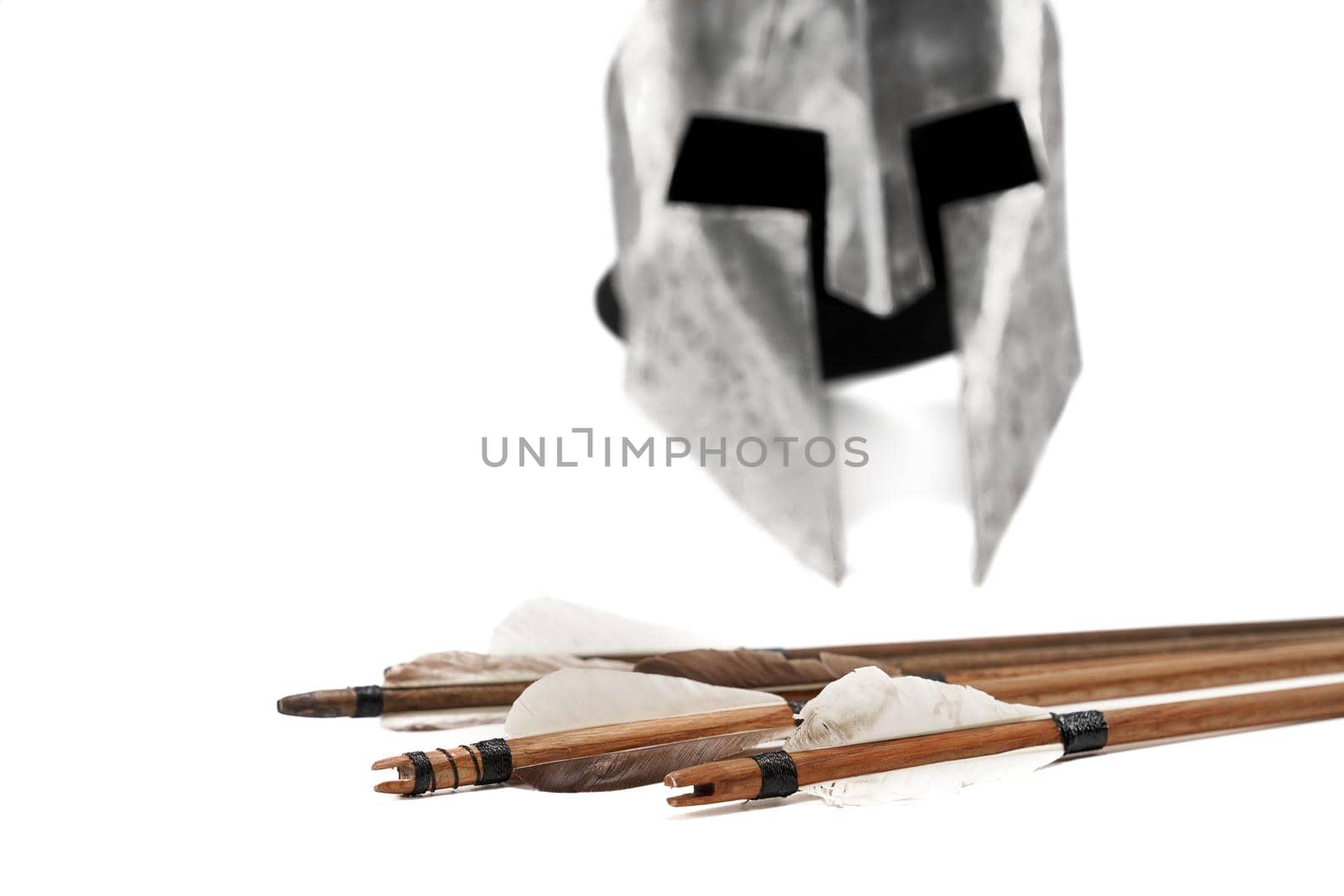 Close up cropped view of ancient metal silver helmet and wooden arrows with grey feathers isolated on white background. Medieval armour and old defensive weapon.