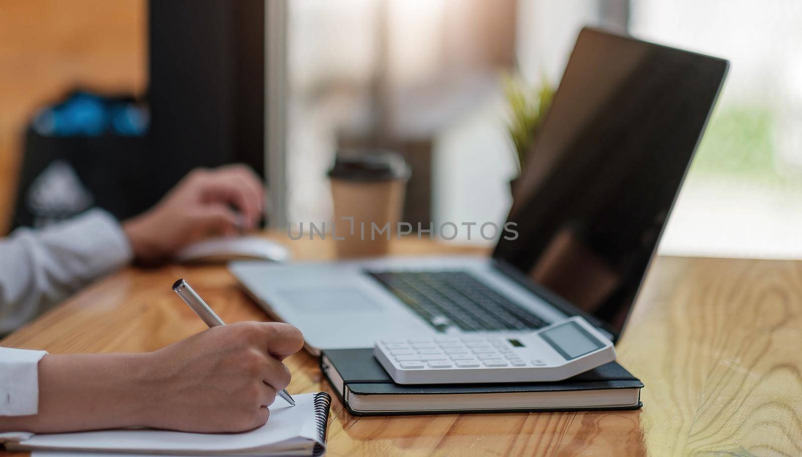 Side view and close up of woman's hands using laptop and writing in notepad. Working on project concept by wichayada