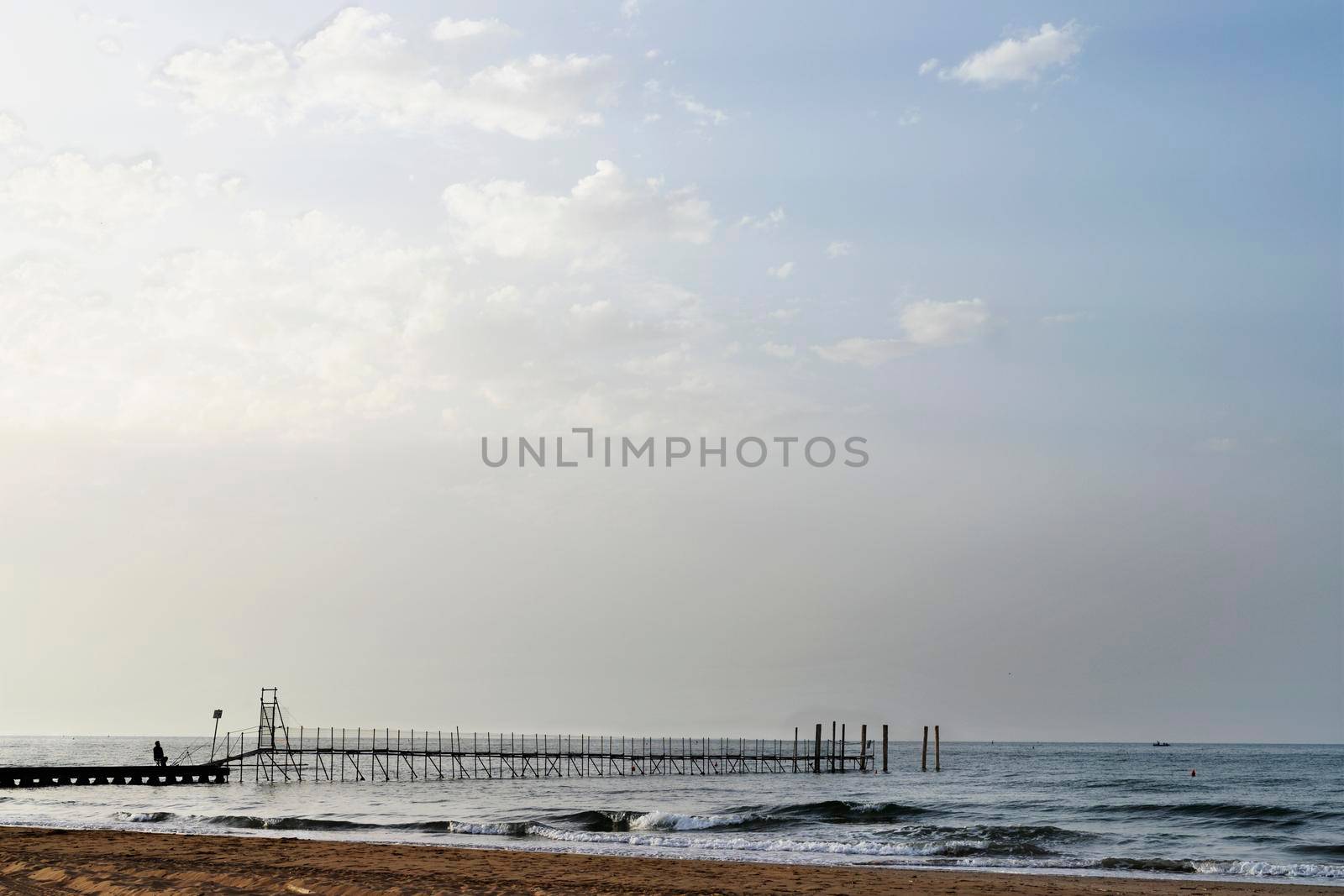 Long wooden pier on the sea , one fisherman , peacefulness