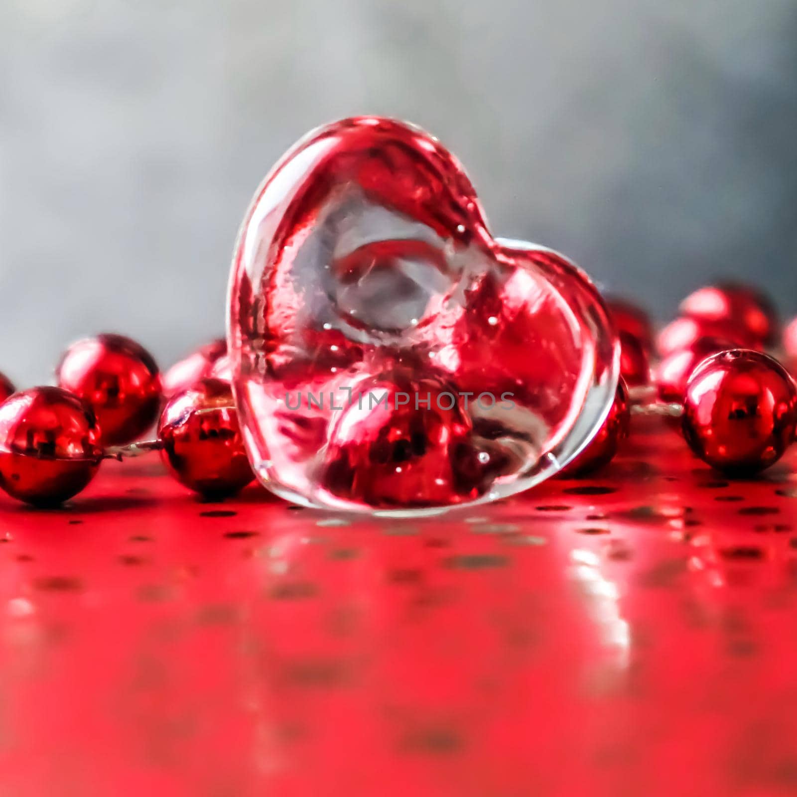 Shining transparent heart and a group of red beads. Perfect Valentine's Day greeting card background. Image in red tone on grey background in a 1x1 format
