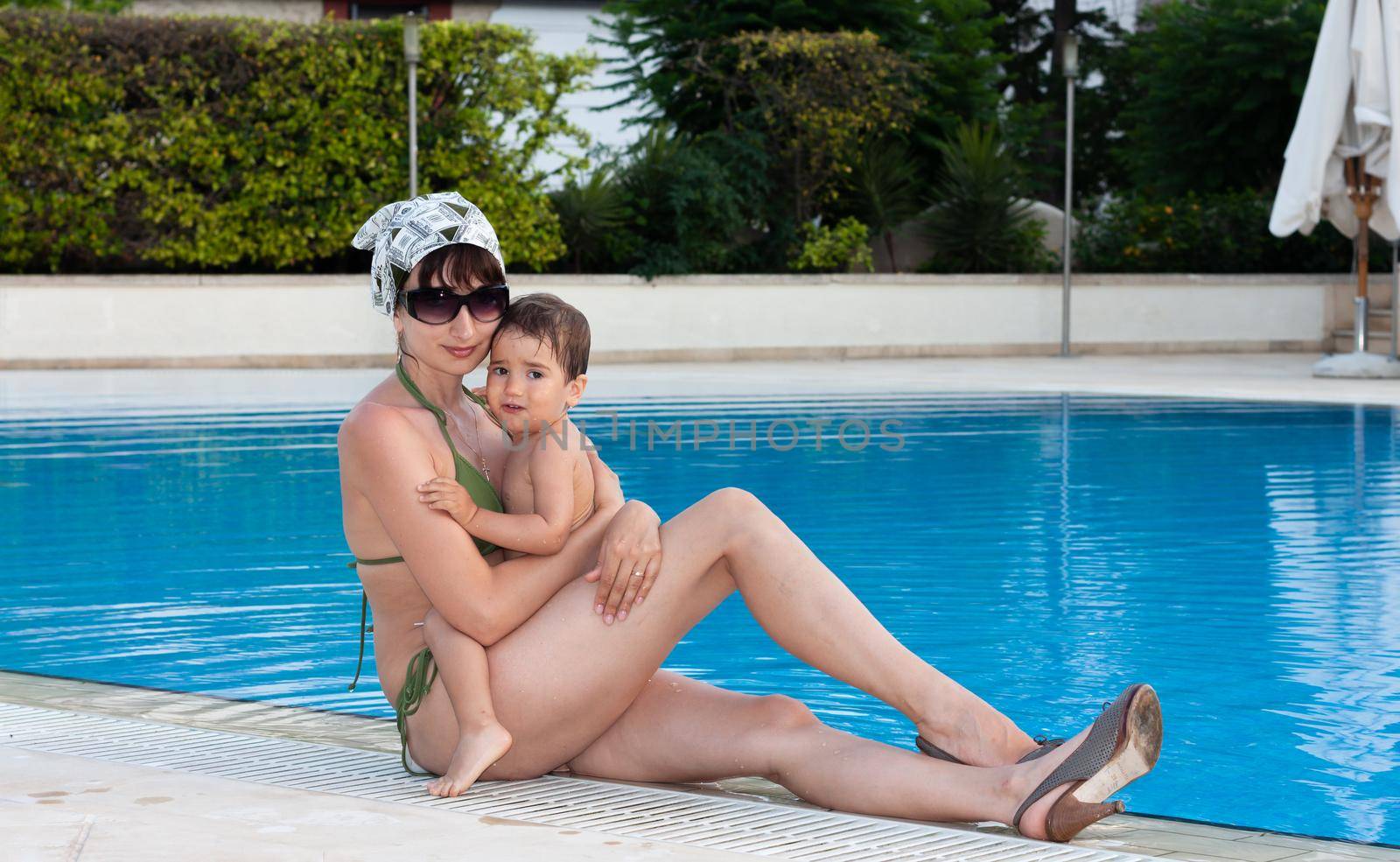 Happy family and healthy lifestyle. Young mother with small child near the pool are resting at the resort