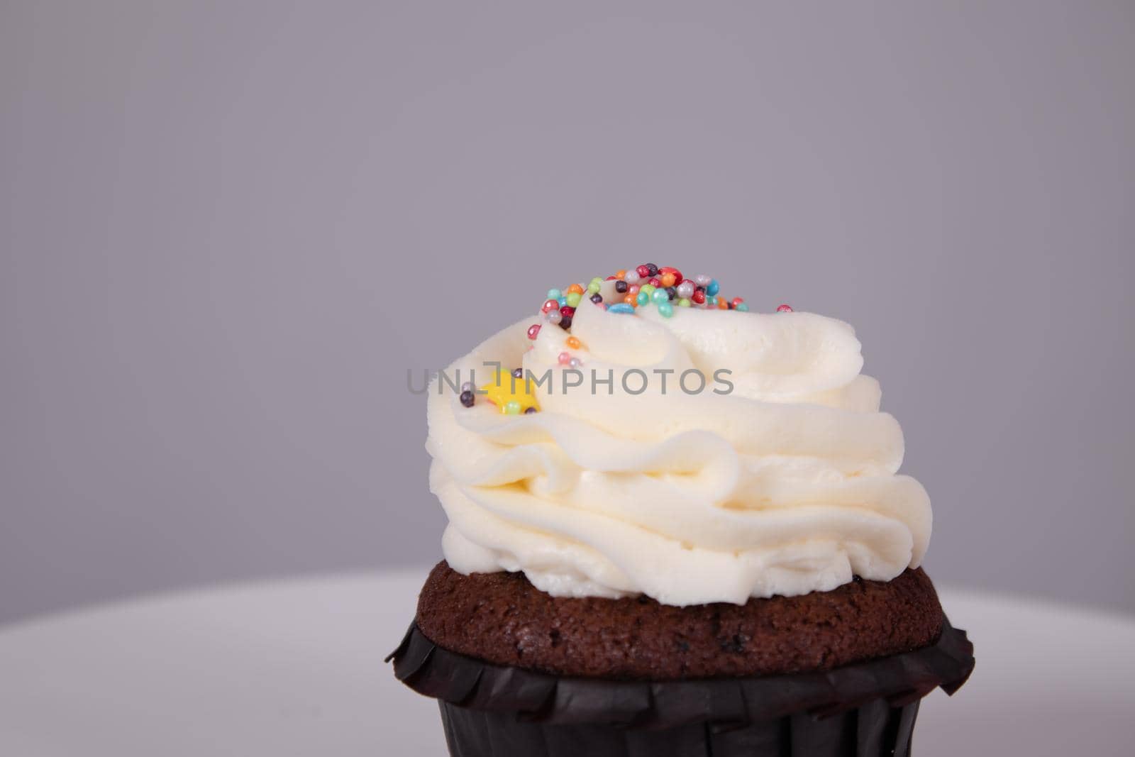 tasty chocolate cupcake with white topping cream on a white stand on a gray background. sweets, bakery. party food. dessert.