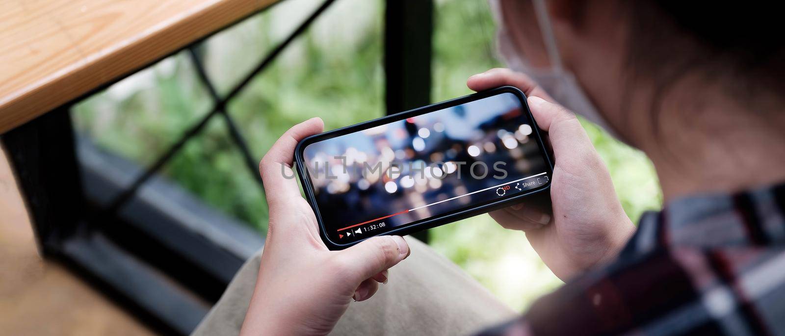 Cropped image of female hand holding smartphone and watching video while standing outdoor. by wichayada