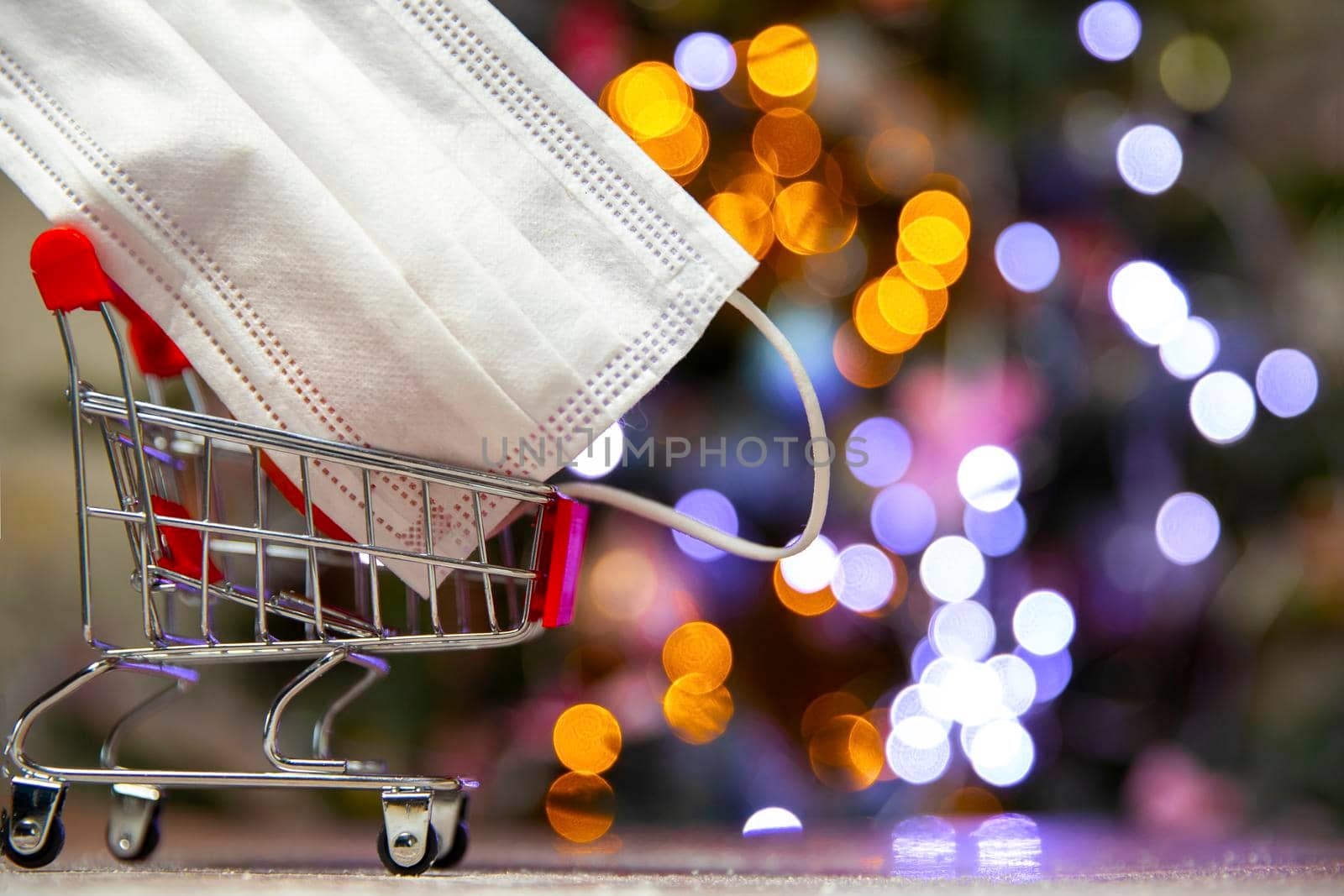 Protective safety mask in iron shopping basket near Christmas tree, Covid-19, coronavirus, holiday concept with copy space and bokeh lights background space for text