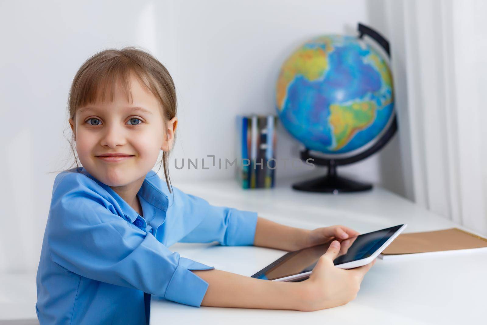 Cute little girl is sitting at table with her laptop and studying online