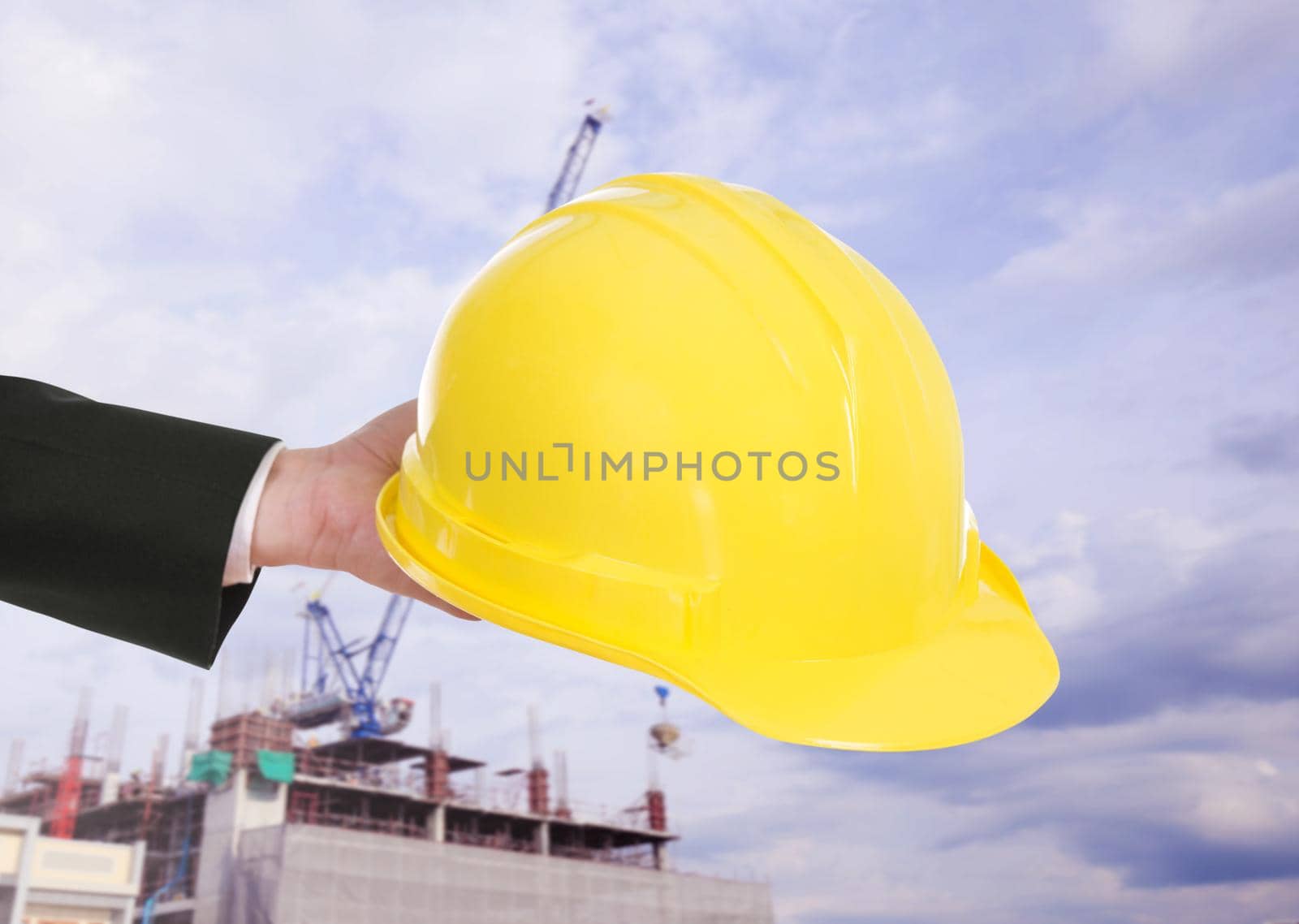 hand of engineer holding yellow helmet with construction crane background