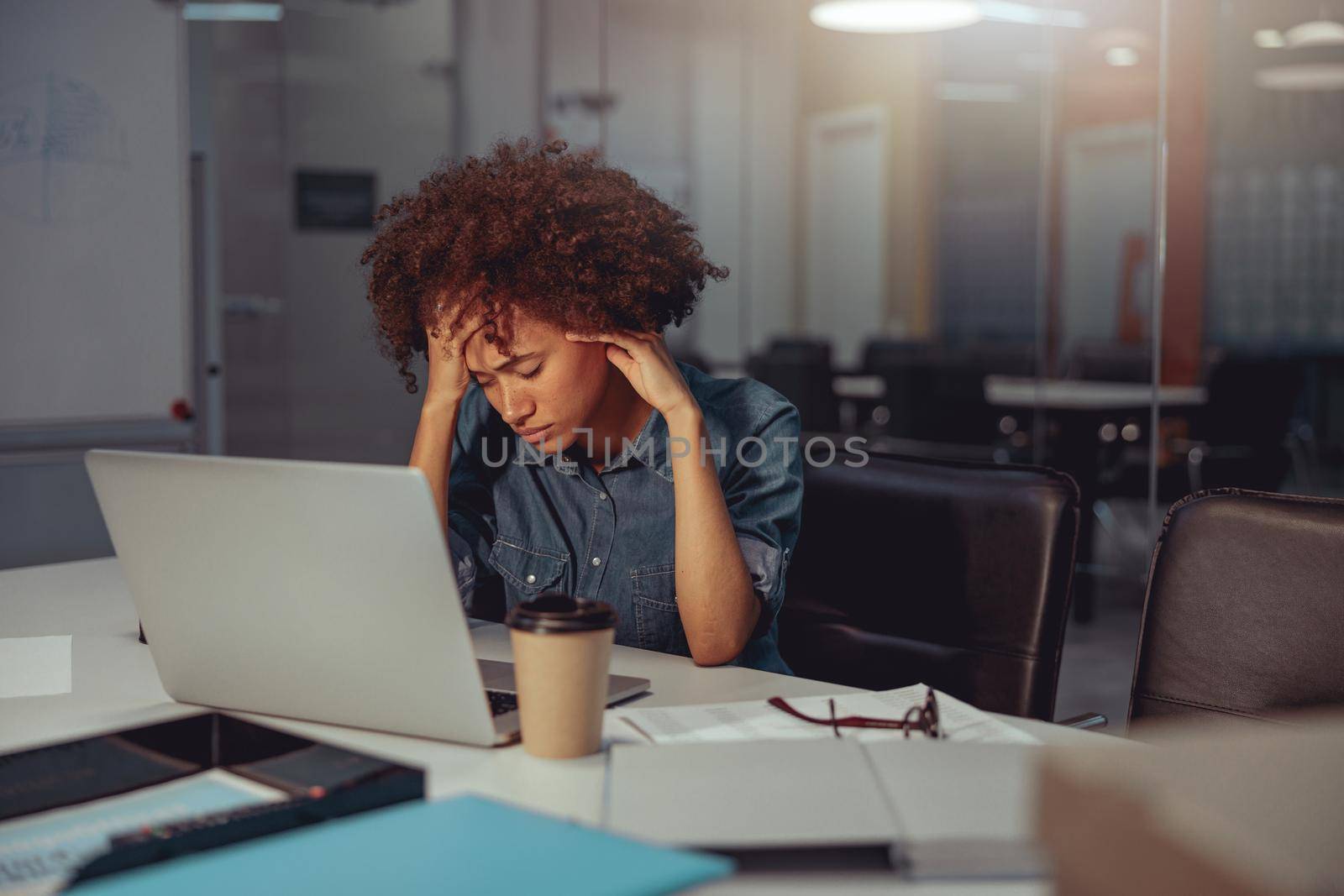 Tired Afro American woman sitting at the desk and using laptop in the office. Business, employment concept