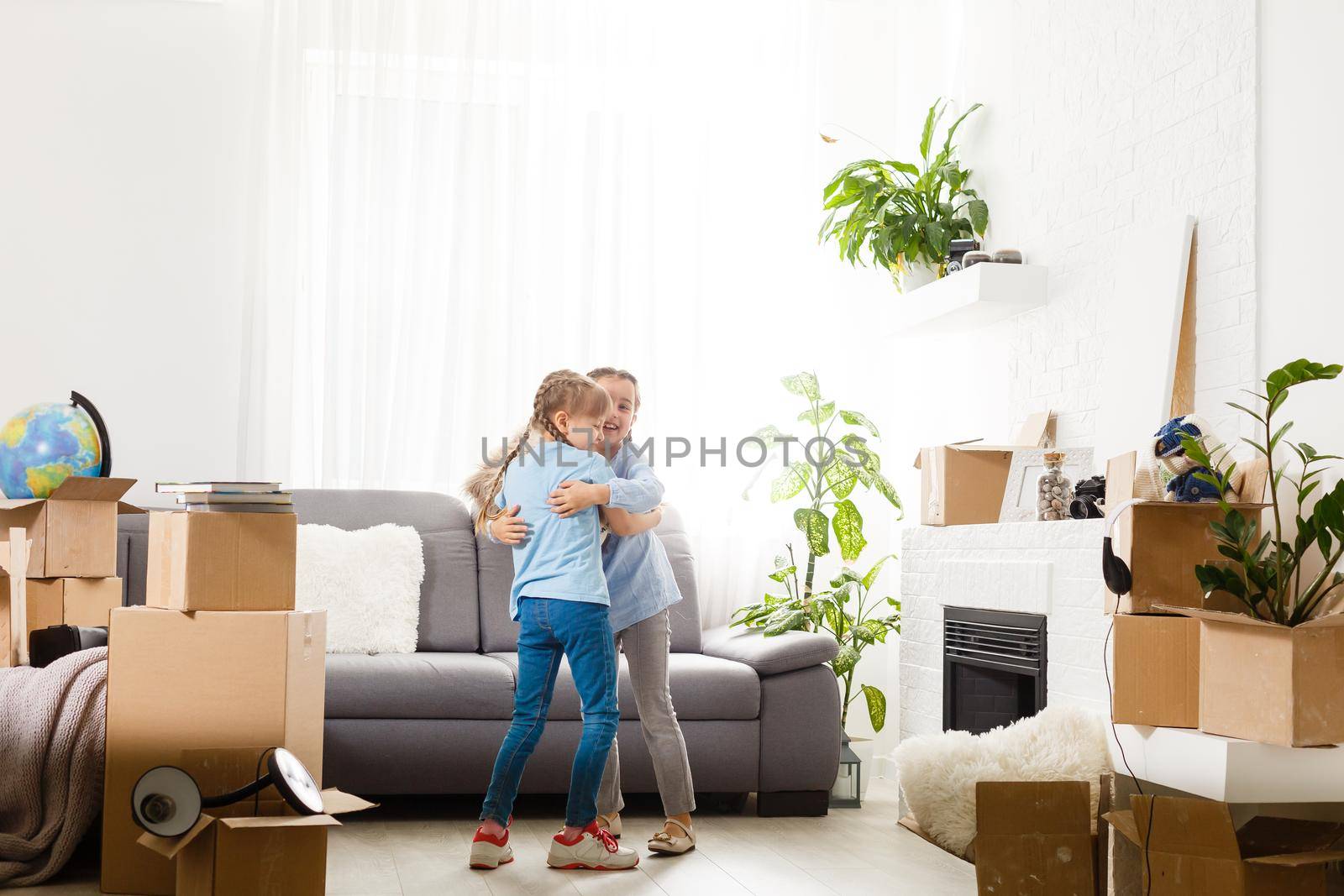 two little daughters celebrating moving day, excited by relocation into new house, laughing living room with cardboard boxes