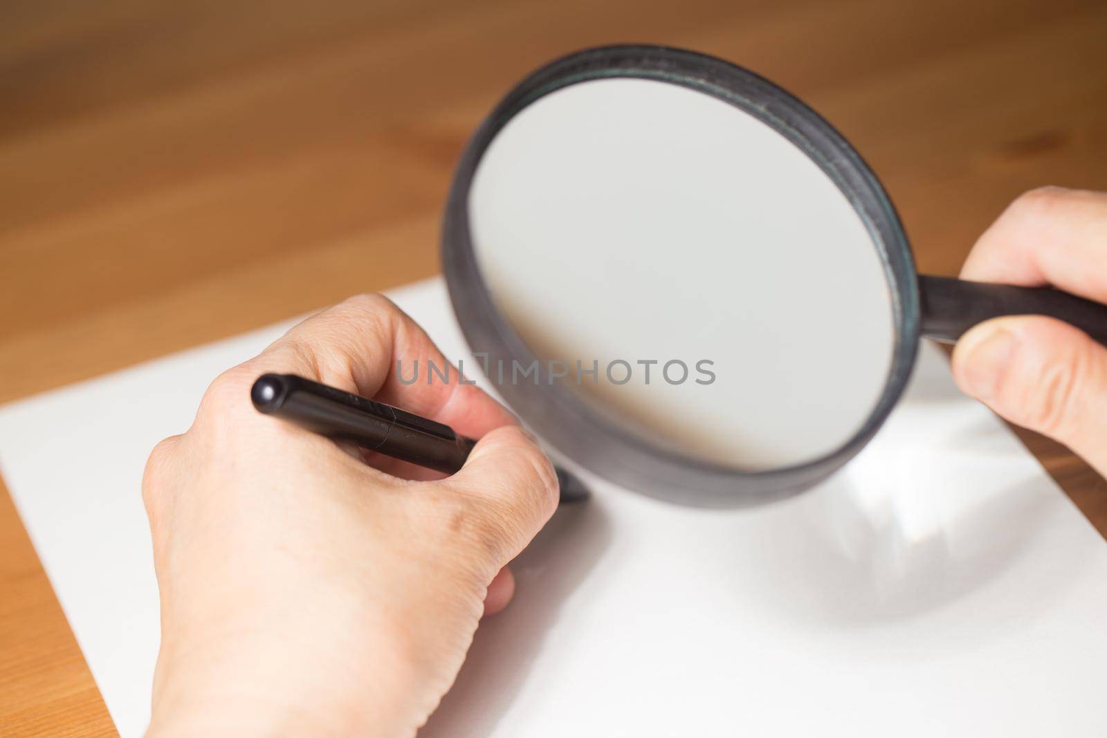 very aged person is writing on a paper with Magnifier