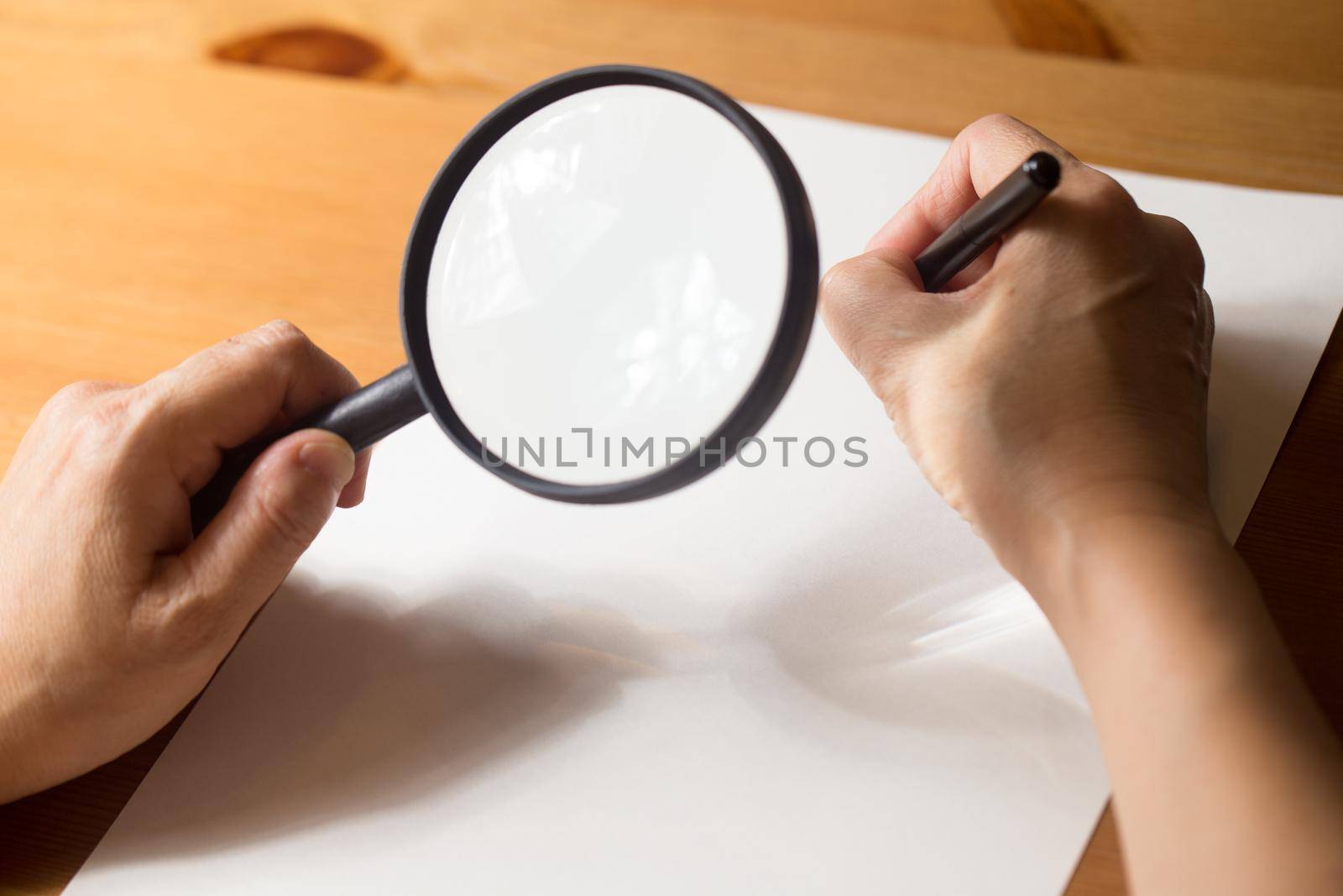 very aged person is writing on a paper with Magnifier