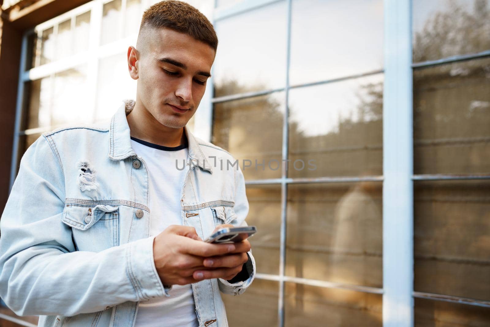 Young urban casual man using smart phone while walking in the street, close up