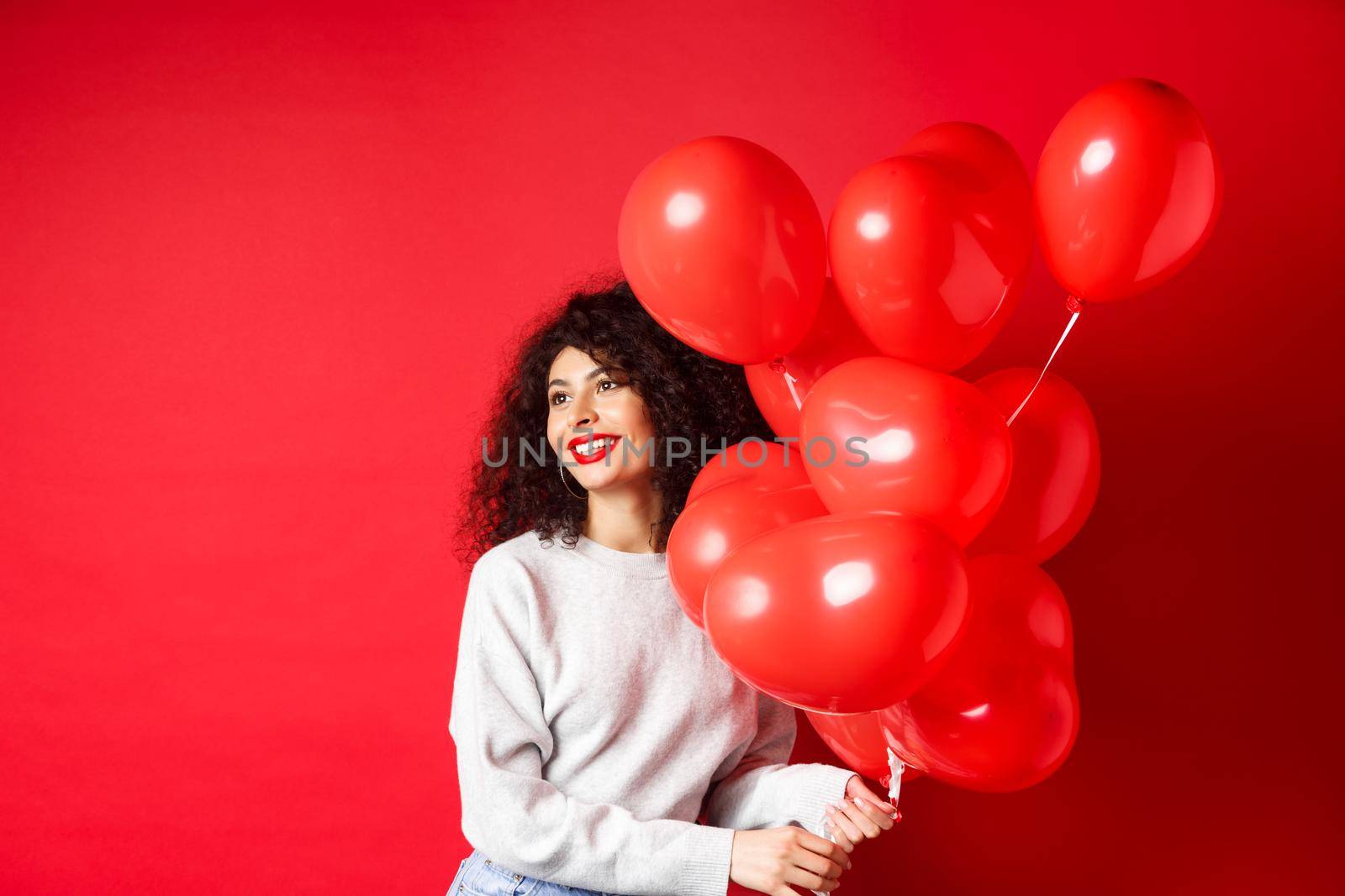 Holidays and celebration. Happy woman posing with party balloons on red background, looking aside at empty space by Benzoix