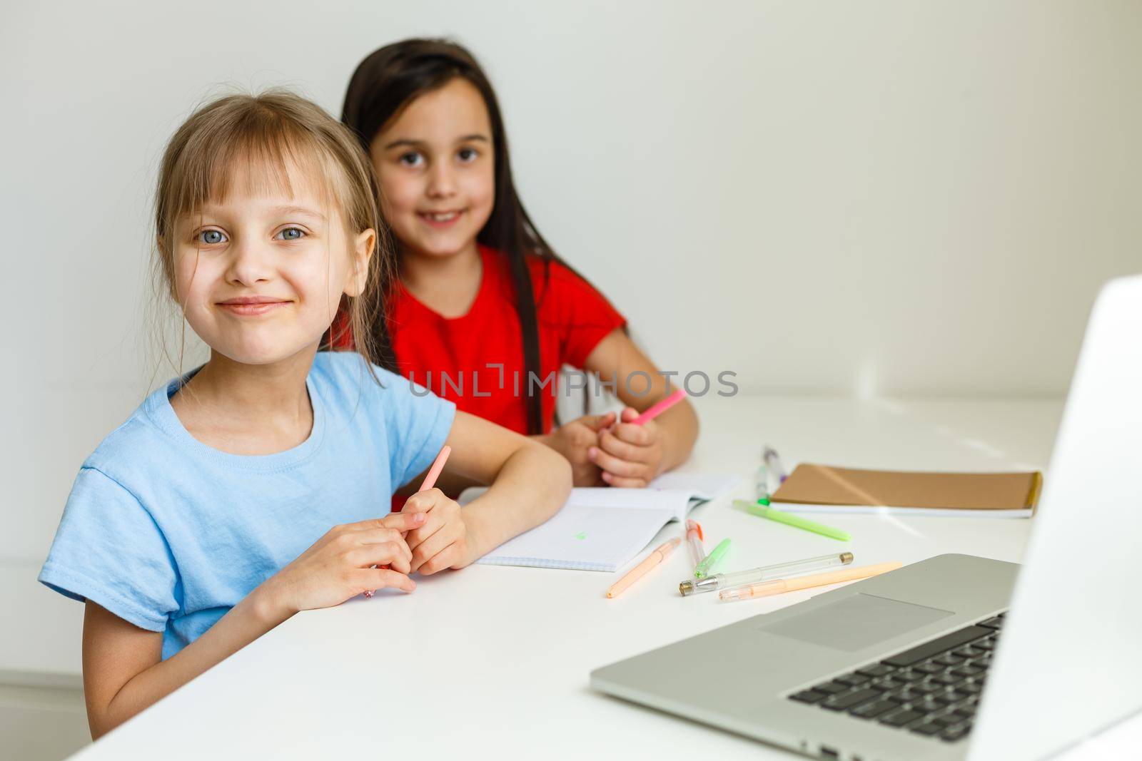 Two girls, the oldest and the youngest, are engaged at a table on a laptop.