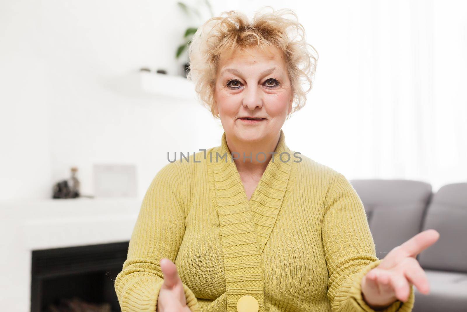 Smiling middle aged mature grey haired woman looking at camera, happy old lady posing at home indoor, positive single senior retired female sitting on sofa in living room headshot portrait