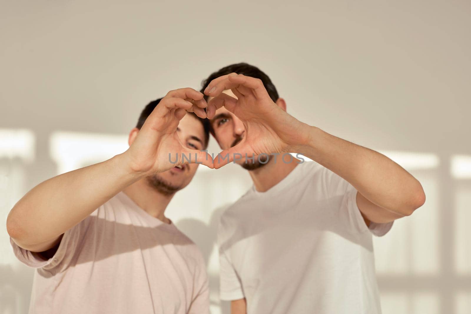 Gorgeous homosexual couple men make heart shape from fingers and palms