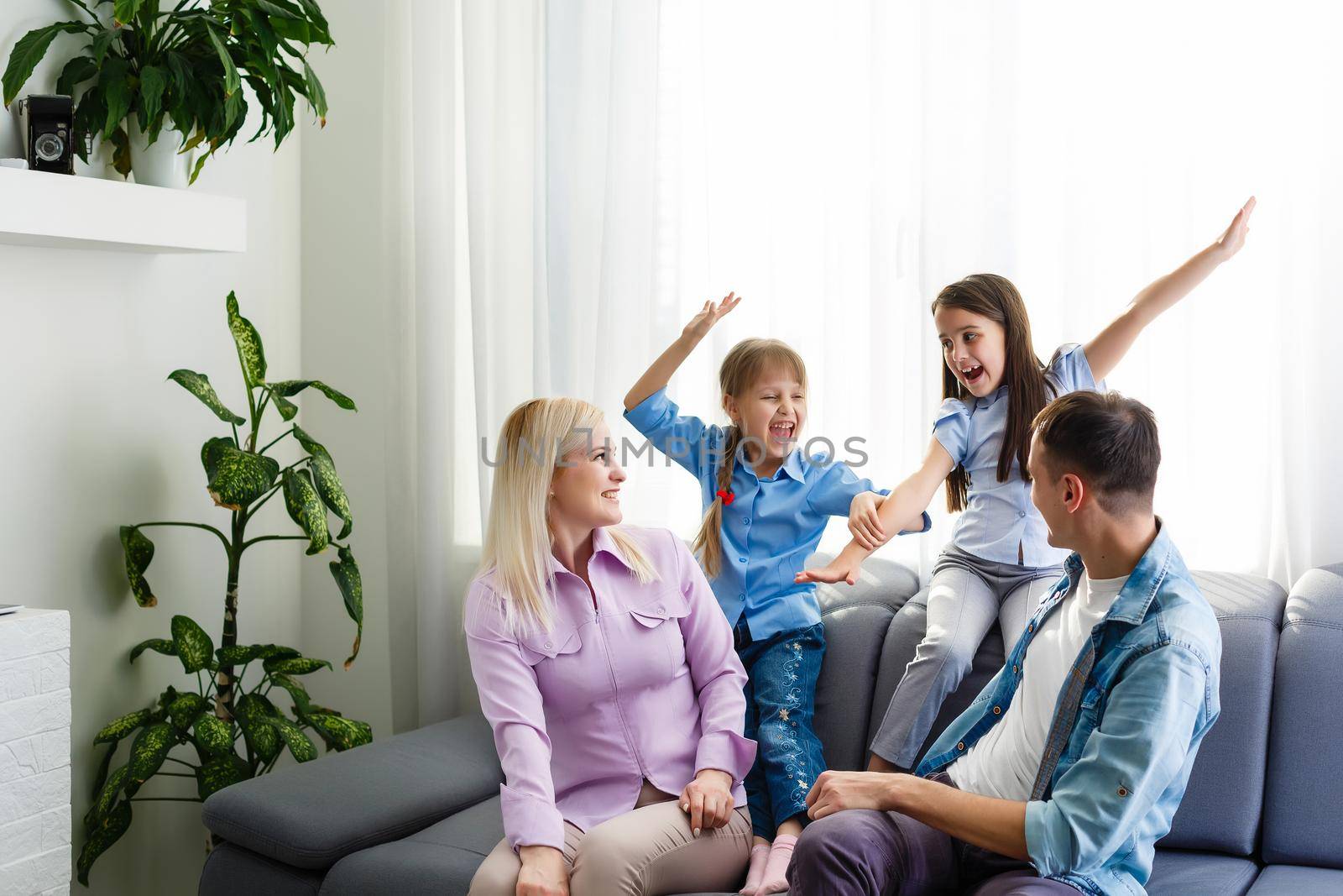 Cheerful young family with kids laughing sitting on couch together, parents with children enjoying entertaining at home