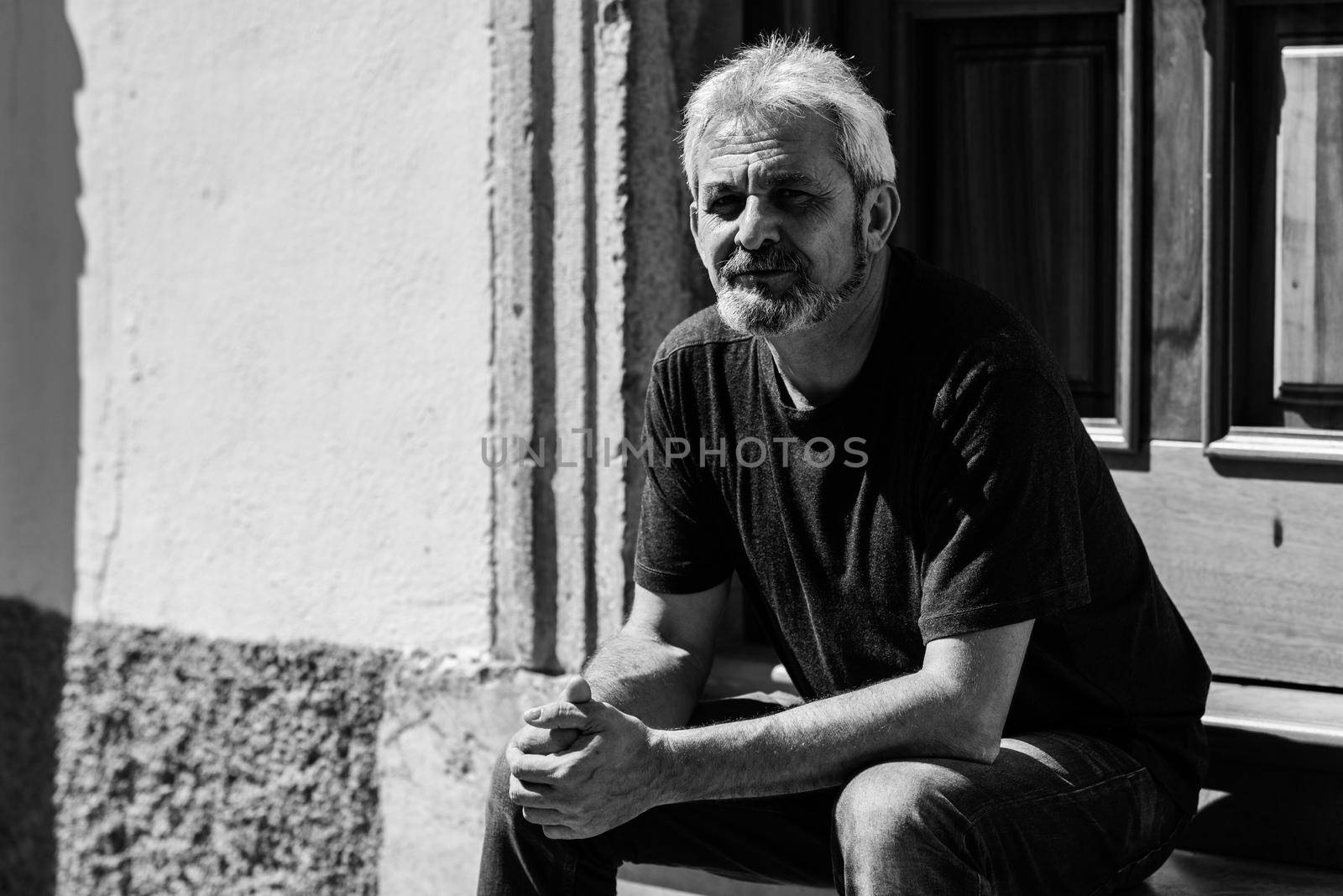 Portrait of a senior man smiling at camera in urban background. Mature male with white hair and beard wearing casual clothes.