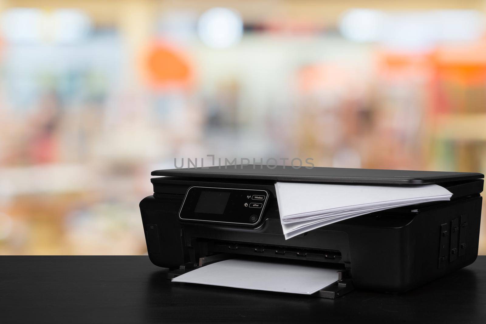 Compact laser printer on black desk against blurred background, close up