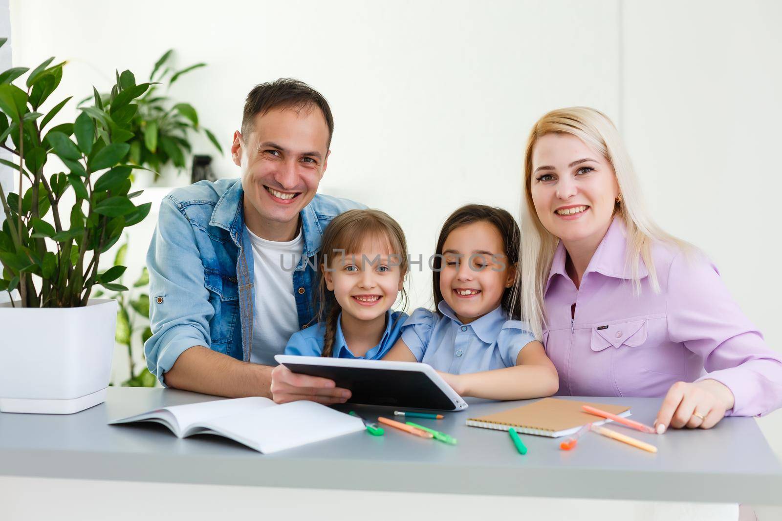 Happy family of four parents and cute little kids children enjoy using the tablet, watching cartoons, make internet video call or shopping online looking at computer screen sit together at home by Andelov13