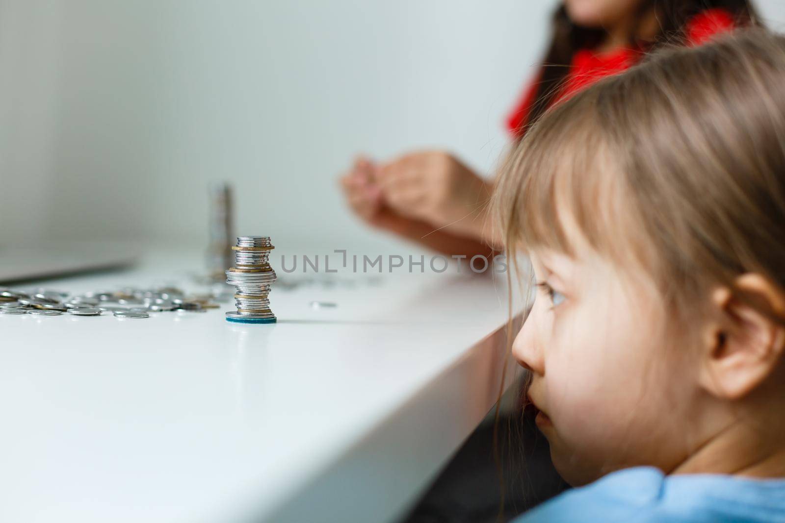 Cute little girl playing with coins making stacks of money, kid saving money for the future concept by Andelov13