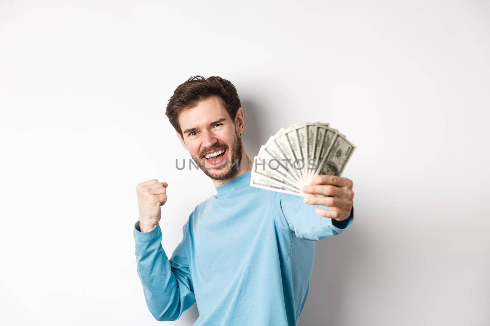 Happy caucasian man stretch out hand with money in dollars, saying yes and celebrating income, got cash prize, standing over white background by Benzoix