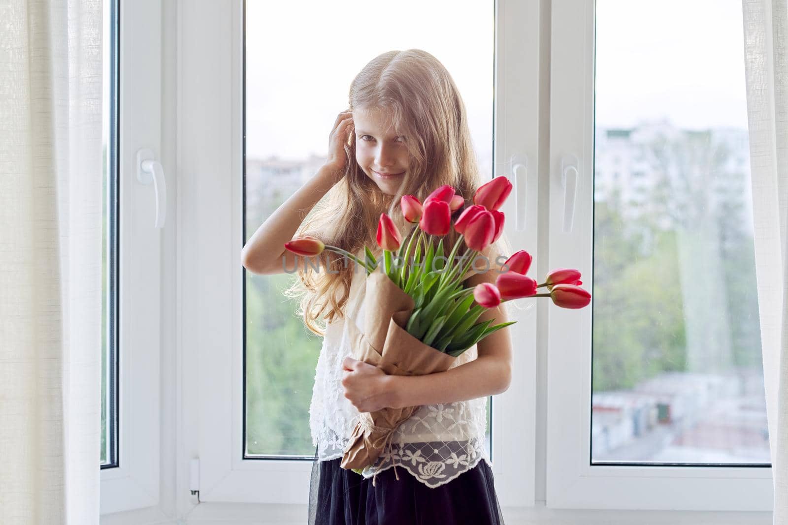 Mother's day, girl child with bouquet of red tulips flowers at home near the window. Gift for mom, love, congratulations, mom's holiday concept