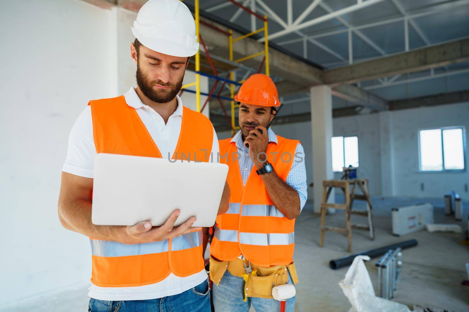 Two specialists supervisors in hardhats using laptop at construction site for work, close up