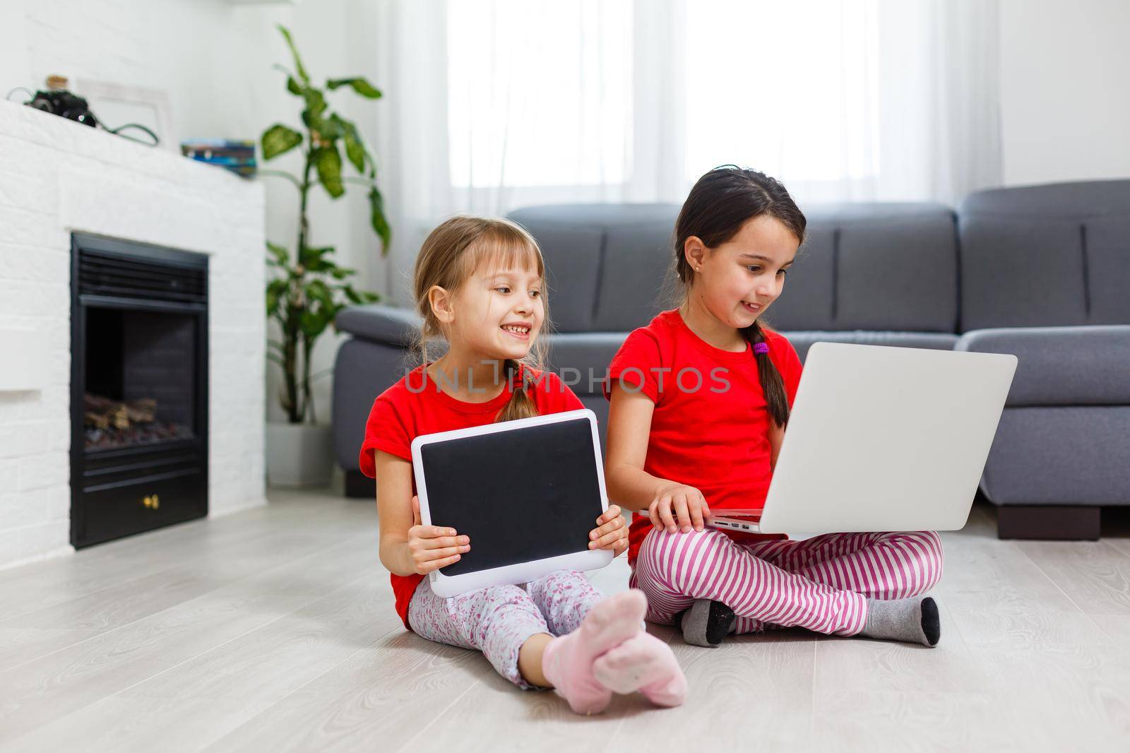 Little girls playing on a tablet computing device sitting on the floor by Andelov13