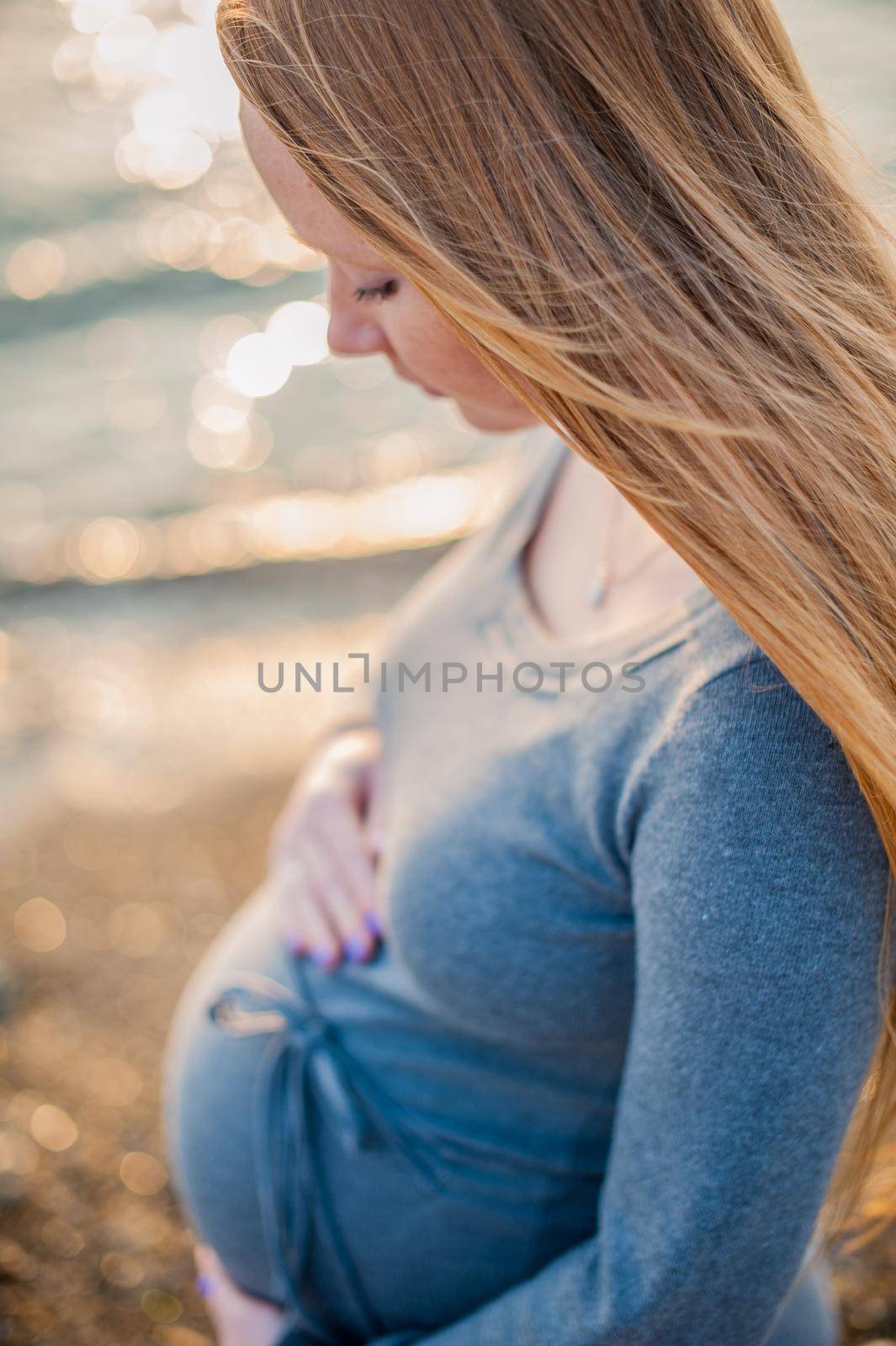 Pregnant young woman standing on the beach in a gray knitted dress. Pregnancy concept by galitskaya
